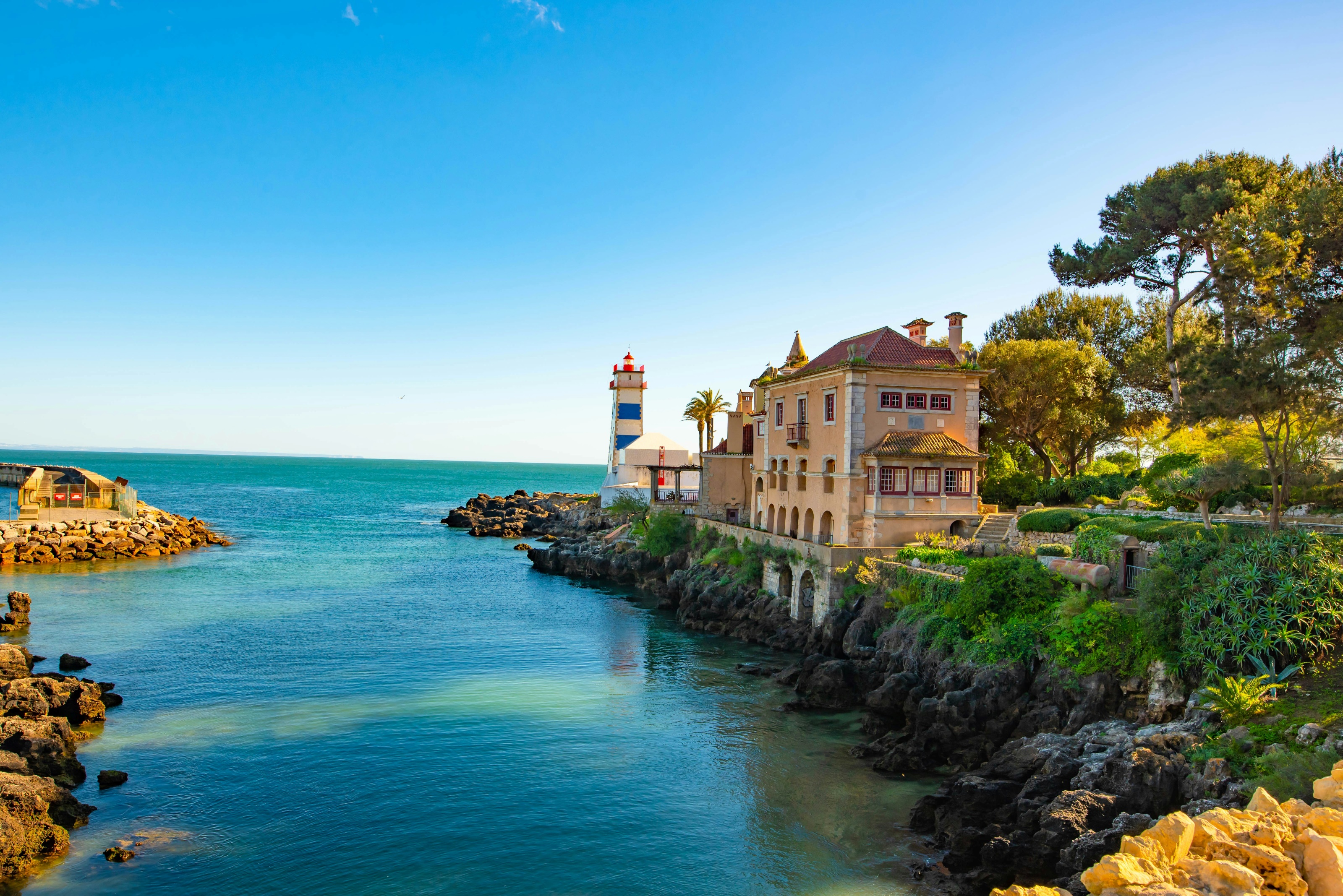 Farol de Santa Marta em Cascais, com edifício à beira-mar rodeado por rochas e natureza, cenário sereno ideal para viver junto ao Atlântico.